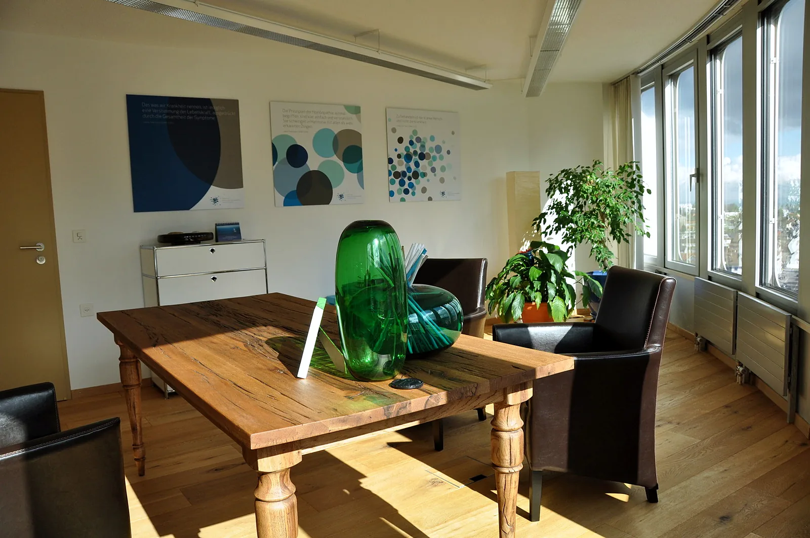 Praxisraum mit Holztisch und grossen Fenstern